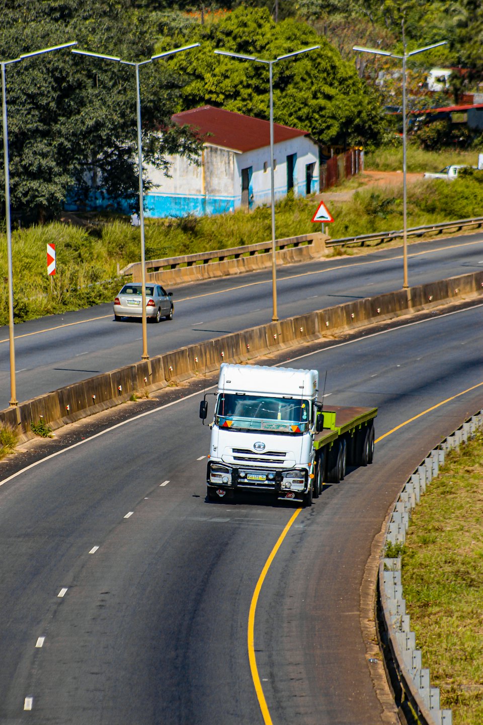 White semi-truck driving on a sunny highway with trees.