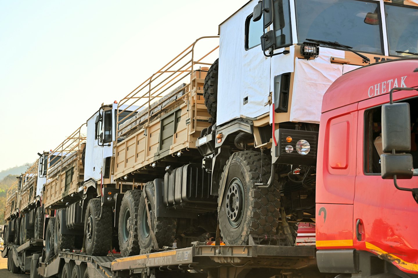 Military cargo trucks loaded onto flatbed trailers for transport.