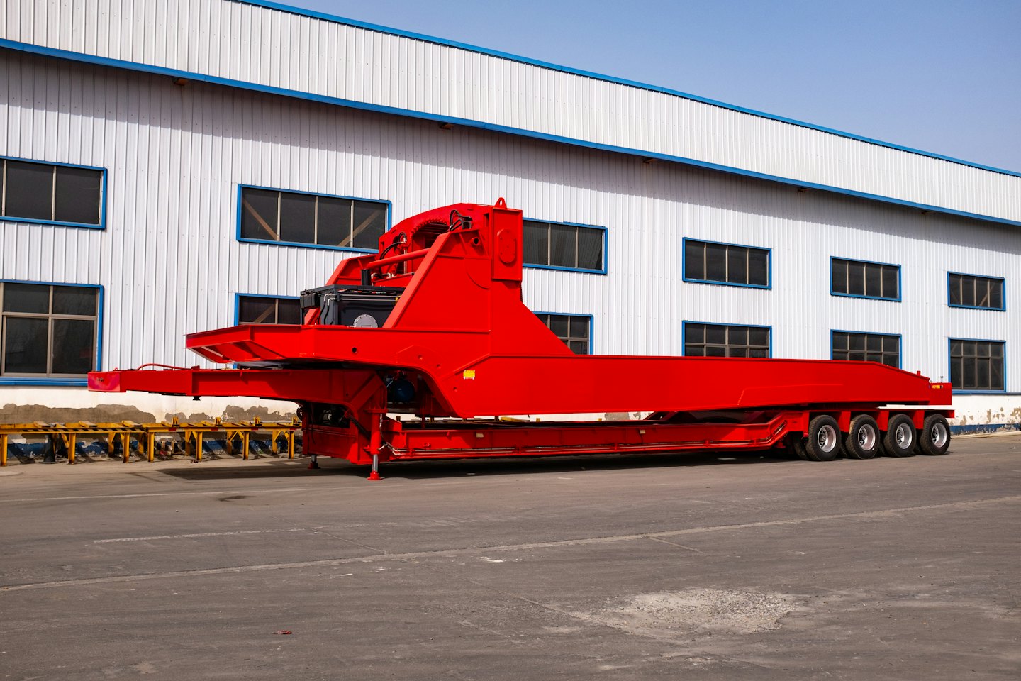 A red flatbed trailer parked in front of an industrial building.