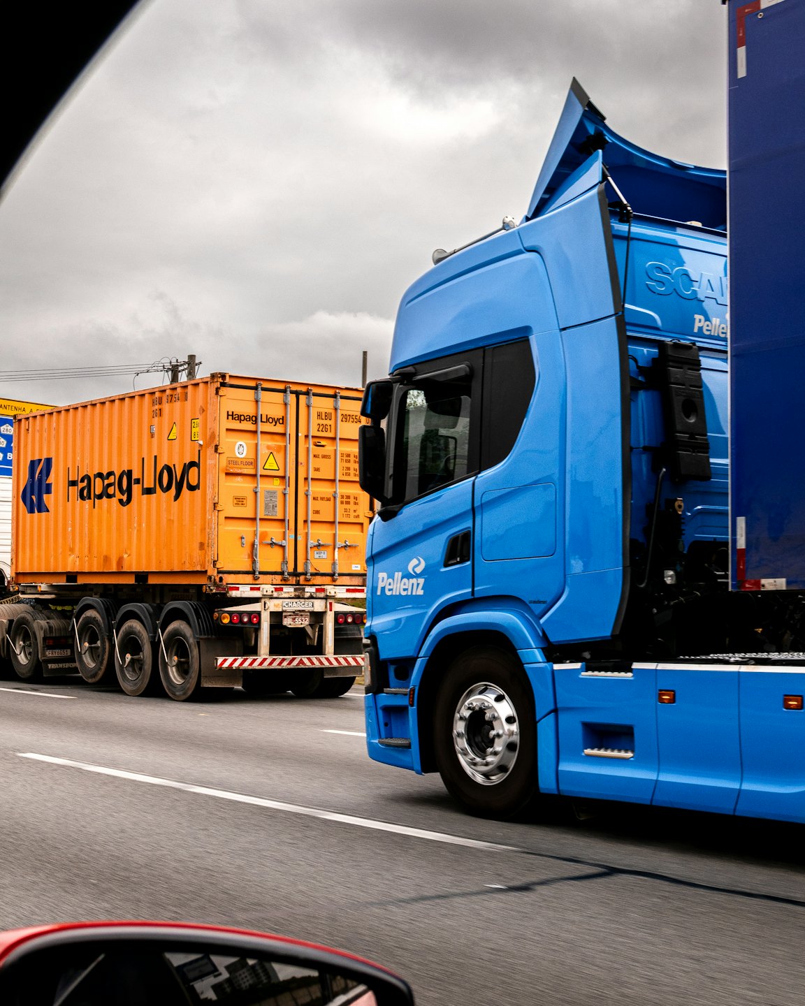 Two commercial trucks driving on a highway under an overcast sky.
