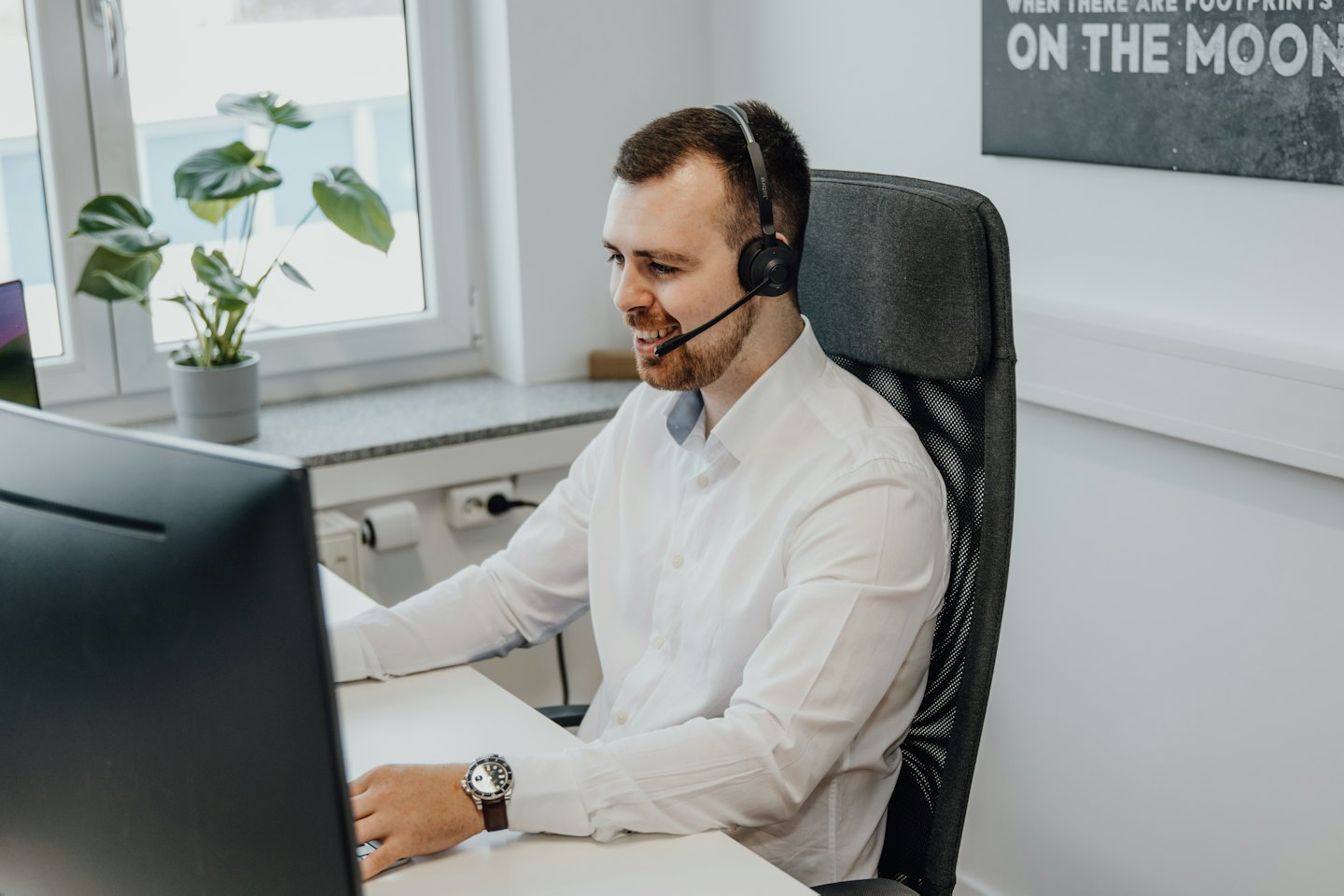 Man in headset smiles while working at a computer.