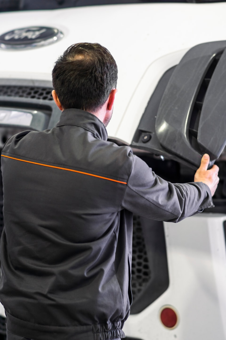 Mechanic inspects large vehicle engine bay holding a grey panel.