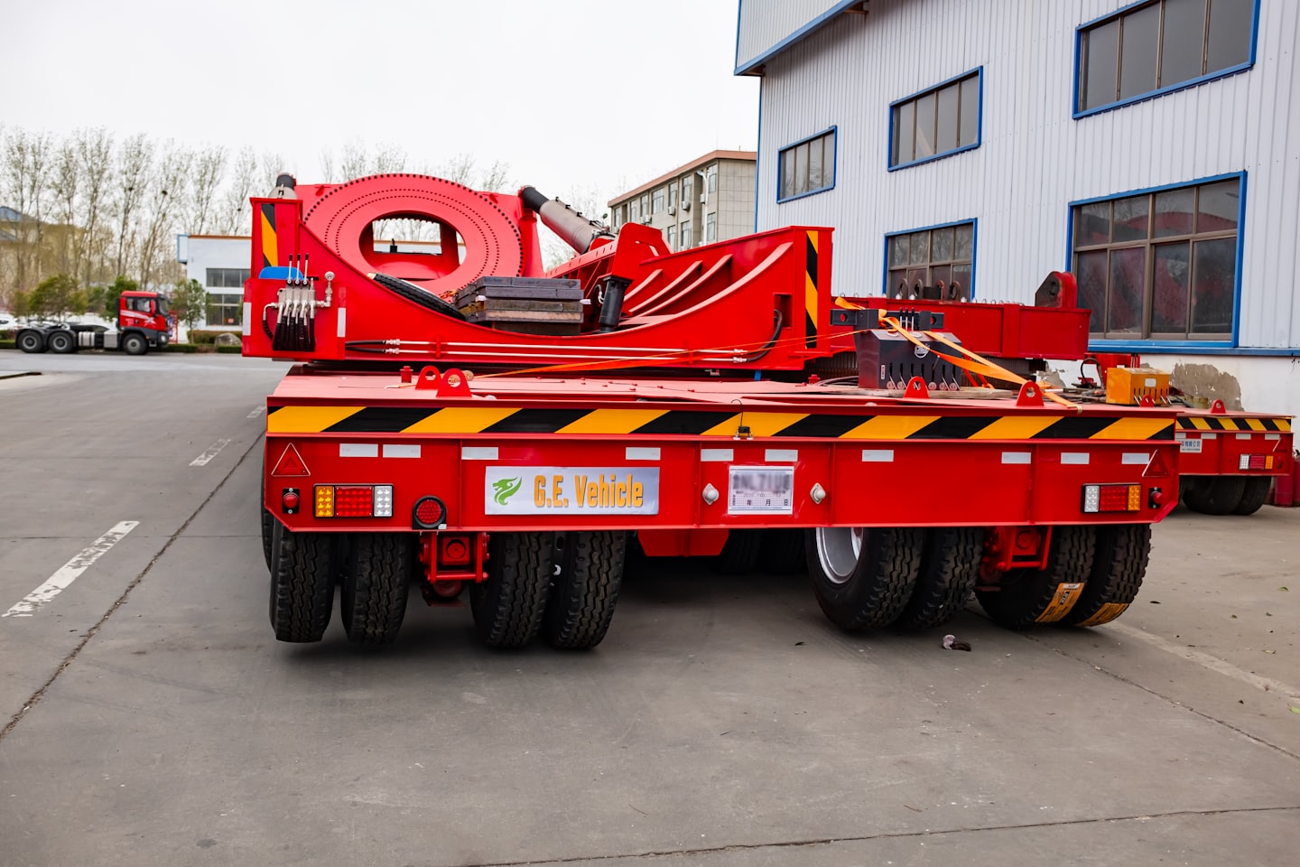 Red flatbed trailer with hydraulic machinery parked in industrial yard.