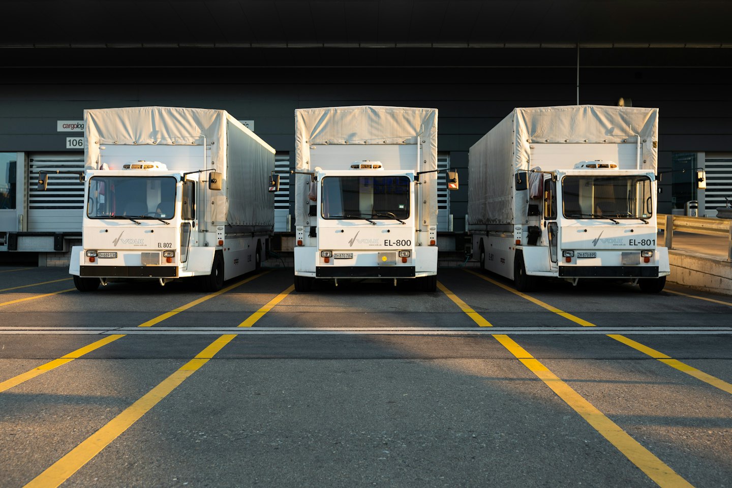 Three white cargo trucks parked at loading docks.